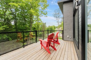 A wooden deck with red Adirondack chairs and a glass balustrade overlooking a forested area. - Chalet Solea by Tremblant Platinum (la conception)