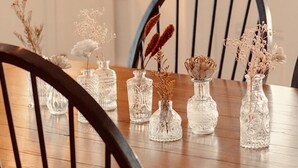 Une table à manger ornée de six vases en verre contenant des fleurs séchées, le tout placé devant un fond en bois.