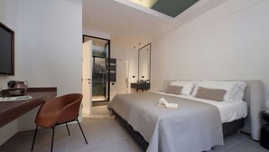 Una habitación de hotel moderna con una cama grande, un escritorio con una silla, un espejo y vistas a la ciudad por la ventana.
