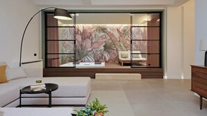 Una sala de estar moderna con un sofá, una mesa de centro, una lámpara y una puerta corrediza de vidrio con estampado de hojas tropicales.