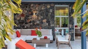 A modern outdoor seating area with a stone wall backdrop, a white sofa, and orange lounge chairs.