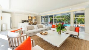 A modern living room with a white sofa, a coffee table, and a view of a swimming pool.