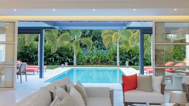 A modern living room with a pool, outdoor seating, and lush greenery.