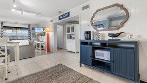Una sala de estar moderna con un cartel que dice 'WELCOME', un espejo grande, una cafetera y un microondas sobre un mueble azul.