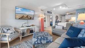 Una sala de estar con decoración temática de playa, que incluye un televisor grande, un sofá a rayas y un mueble consola con adornos.