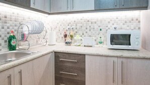 A kitchen with grey cabinets, a white tiled backsplash, a dish rack, a microwave, and a bottle of Fairy dish soap. - Spacious and Luxurious Apart Athens Center by MPS (Athina)