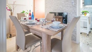 A dining area with a wooden table set for four, surrounded by chairs. A stone wall and a kitchen area are visible in the background. - Spacious and Luxurious Apart Athens Center by MPS (Athina)