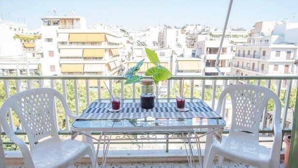 A balcony with two white plastic chairs, a glass table, and two drinks. - Spacious and Luxurious Apart Athens Center by MPS (Athina)