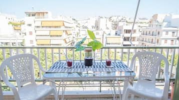 A balcony with two white plastic chairs, a glass table, and two drinks.