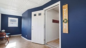 A hallway with a blue wall, a white door, a welcome sign, and a bench. - Spacious Group Home with Arcade (Champaign)