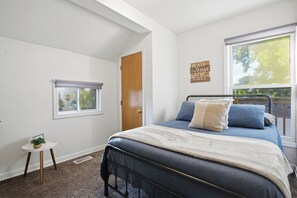 Ein Schlafzimmer mit einem Bett, einem Fenster, einer Tür und einem kleinen Tisch mit einer Pflanze.