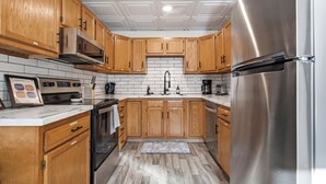 A kitchen with wooden cabinets, a stainless steel refrigerator, a microwave, and a tiled backsplash.
