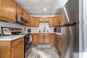 A kitchen with wooden cabinets, a stainless steel refrigerator, a microwave, and a tiled backsplash. - Spacious Group Home with Arcade (Champaign)