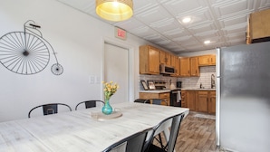 A dining area with a white table, black chairs, a vase with yellow flowers, and a wall-mounted bicycle decoration. - Spacious Group Home with Arcade (Champaign)