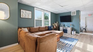 A living room with a sectional sofa, a flat-screen TV, a window, and a small table with decorative items. - Spacious Group Home with Arcade (Champaign)
