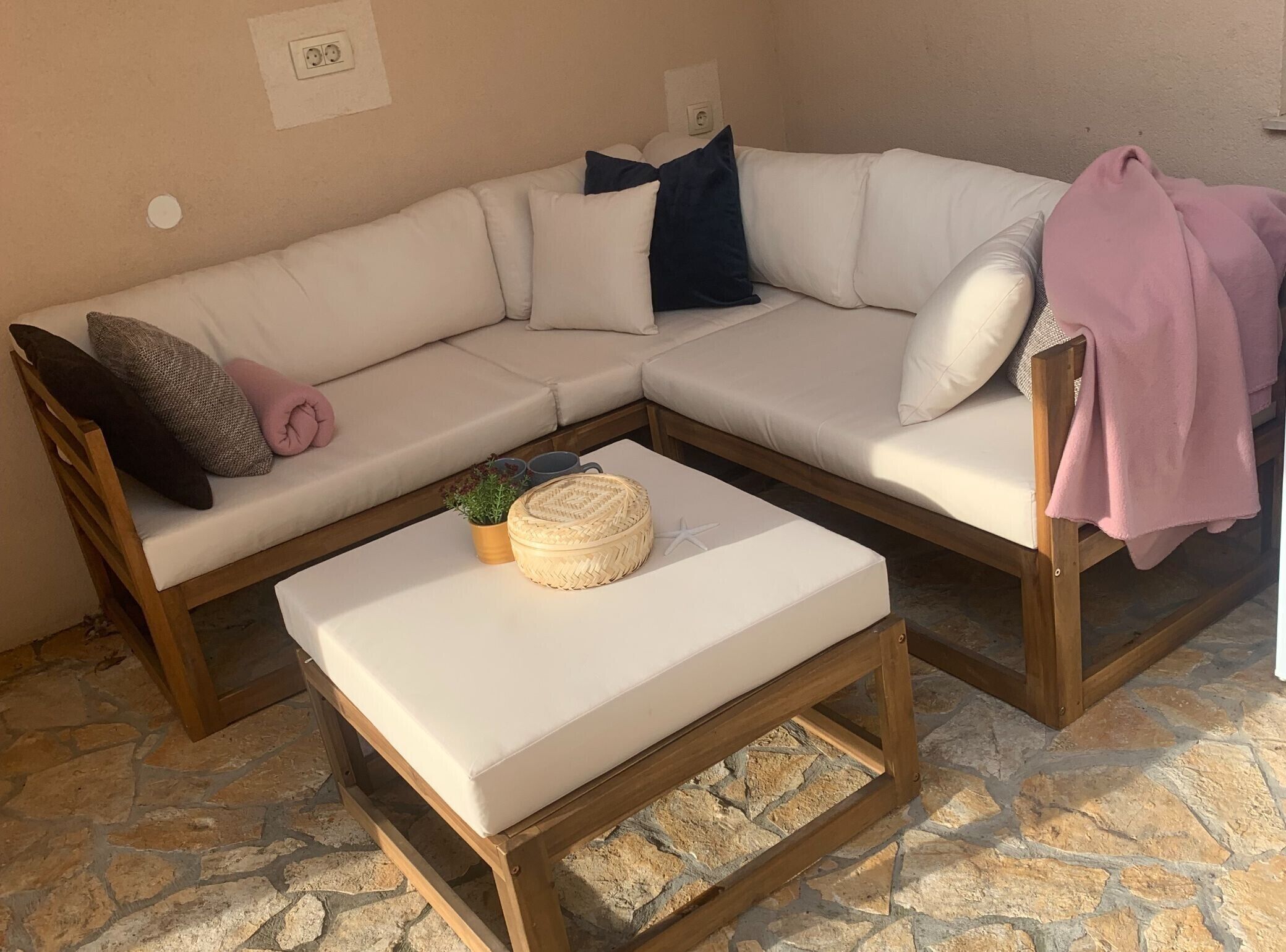 Un sofá seccional en forma de L con cojines, una mesa de centro de madera y una pequeña planta en maceta.
