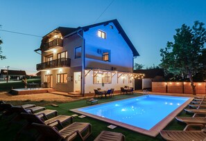 Une maison à deux étages avec une piscine, un espace extérieur aménagé pour s’asseoir et une terrasse bien éclairée.