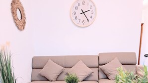 A living room with a beige sofa, a round coffee table with a potted plant, a glass candle holder, and a wall clock. - Apartments Villa Mavi - Two Bedroom Apartment First Floor (Karlovac)
