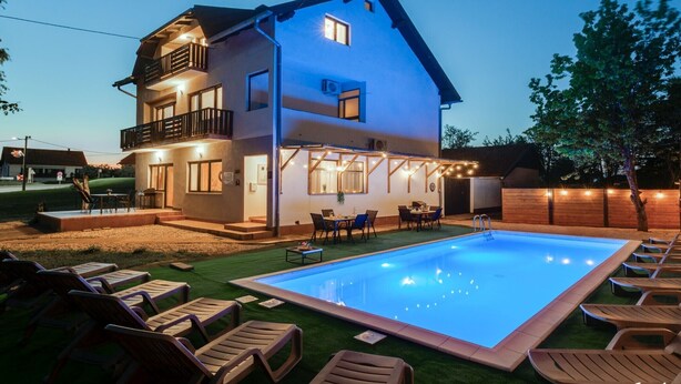 Une maison à deux étages avec une piscine, un espace extérieur aménagé pour s’asseoir et une terrasse bien éclairée.
