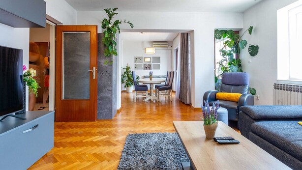 A modern living room with a sofa, coffee table, and TV. There is a dining area in the background with chairs and a table. - Three Bedroom Apartment with Private Pool (Zadar)