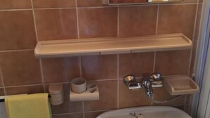 A bathroom with a white sink, a wooden shelf, and a mirror.