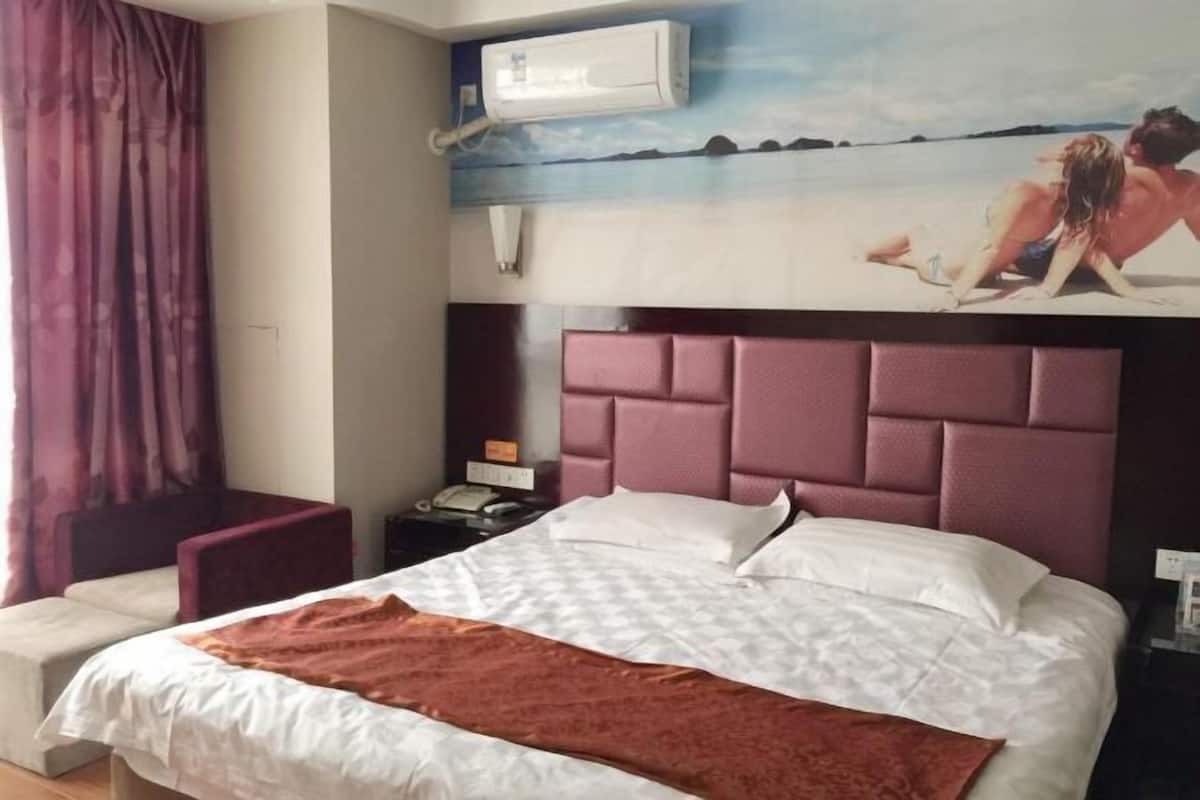 A hotel room with a large bed, a headboard, a nightstand, a telephone, and a wall-mounted air conditioner.