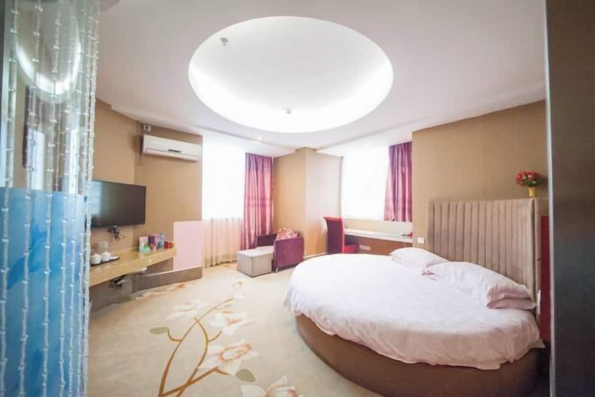 A hotel room with a large bed, a flat-screen TV, a desk with a chair, and a window with curtains.