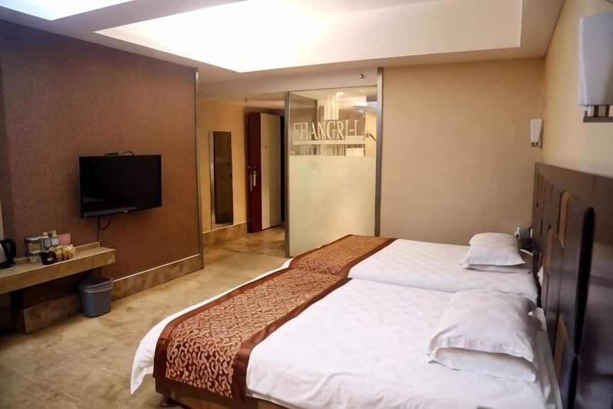 A hotel room with a bed, a TV, a mirror, and a bathroom visible through an open door.