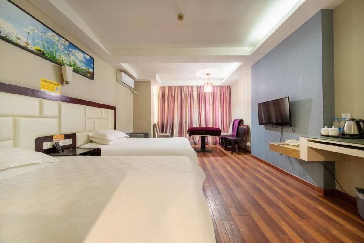 A hotel room with two beds, a desk with a chair, a television, and a window with curtains.