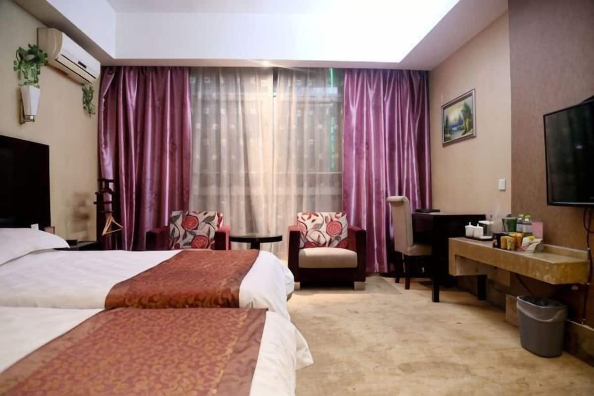 A hotel room with two beds, a desk, a chair, a TV, and a window with curtains.
