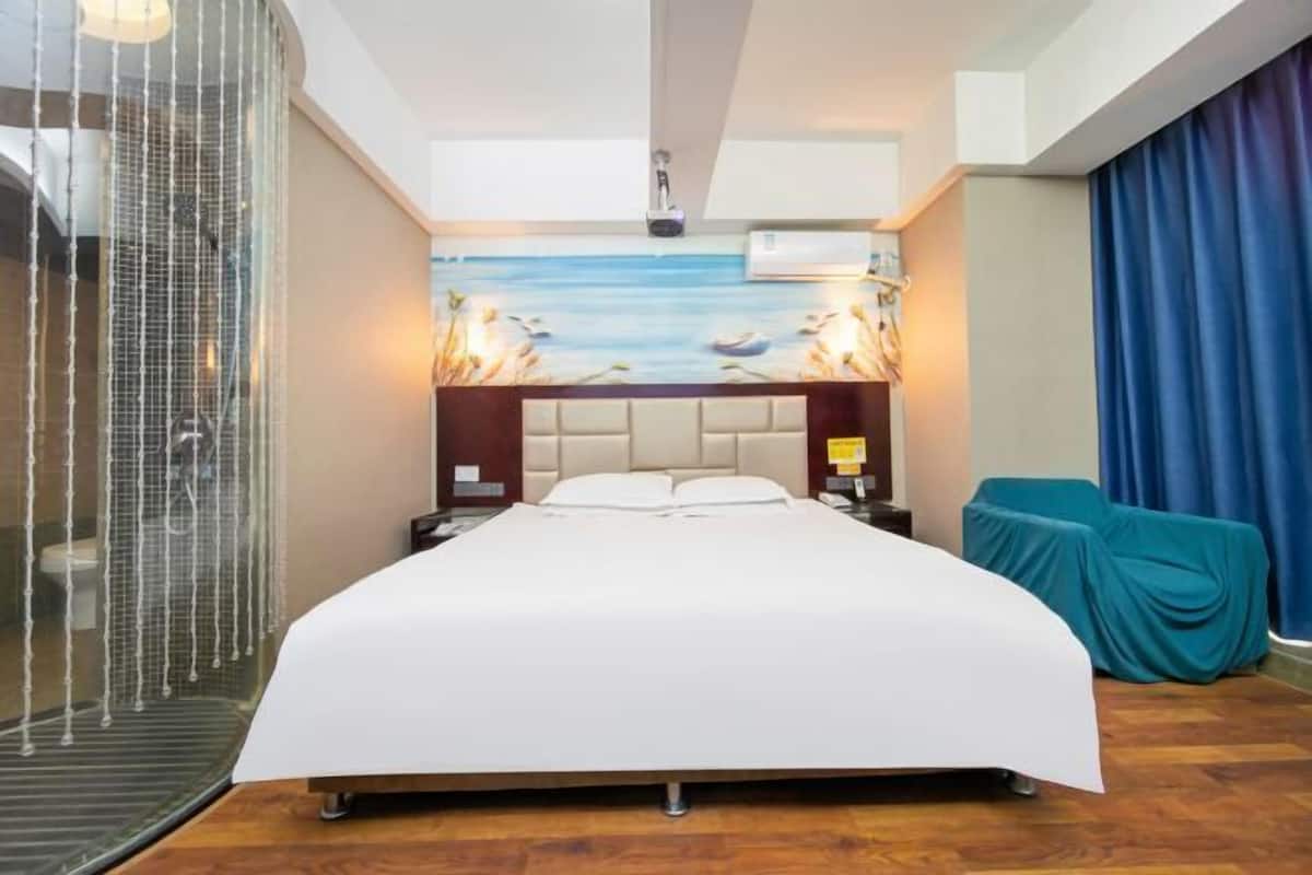 A hotel room with a bed, a shower enclosure, a wall-mounted air conditioner, and a view of the sea.