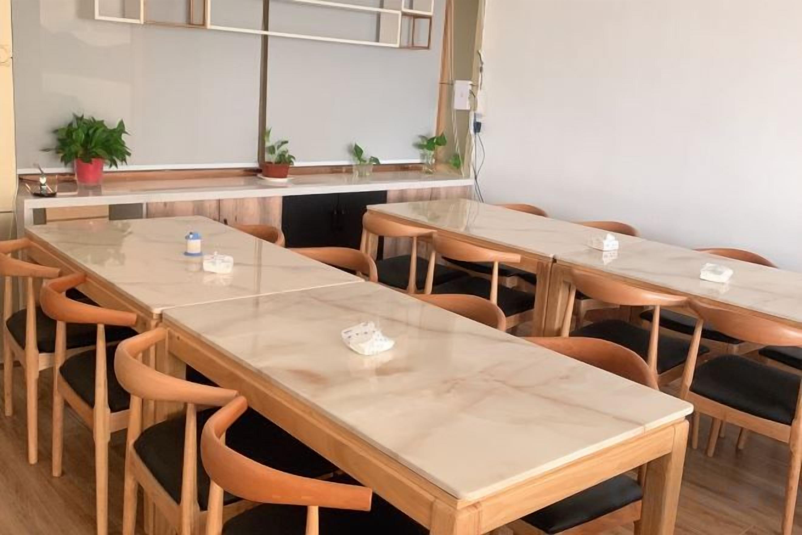 Een vergaderruimte met meerdere tafels en stoelen, een whiteboard en potplanten.