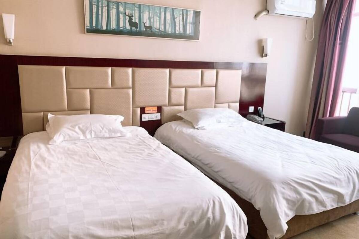 A hotel room with two beds, a headboard, a painting, a nightstand, and a chair.