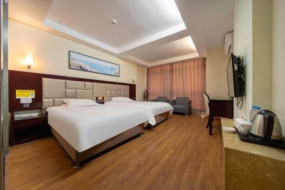 A hotel room with two beds, a desk, a chair, a television, and a coffee maker.