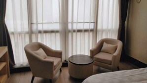 Quarto de hotel com duas poltronas, uma mesa redonda pequena e uma cama.