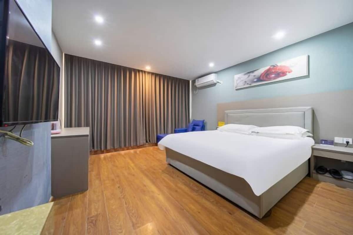 A hotel room with a bed, a desk, a chair, a wardrobe, and a wall-mounted air conditioner.
