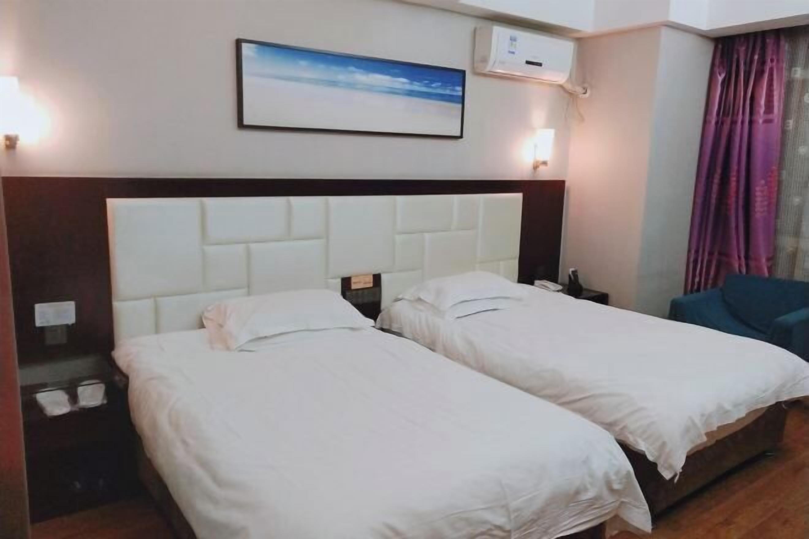 A hotel room with two single beds, a wooden headboard, a nightstand, a lamp, a framed picture on the wall, and a window with curtains.