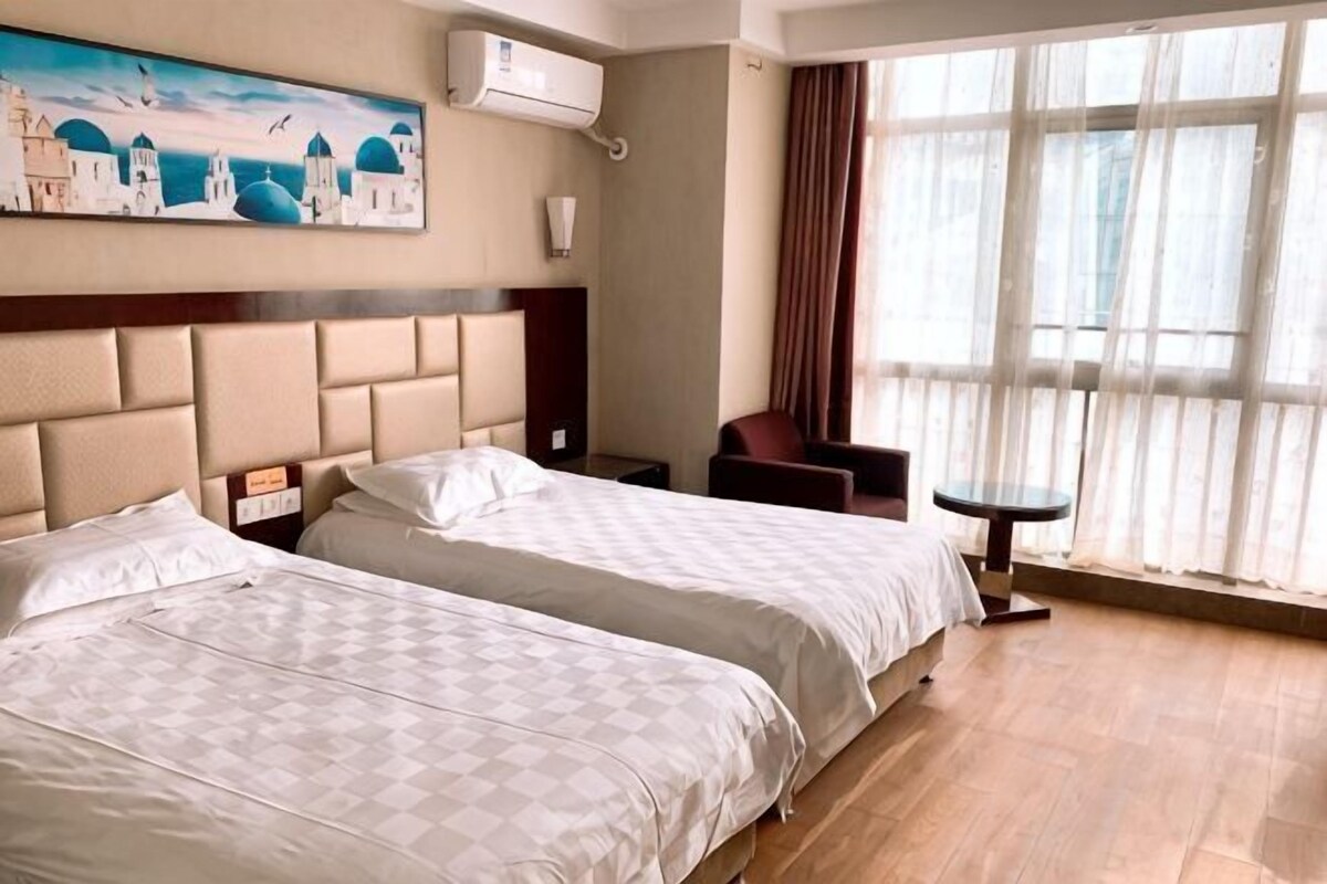 Camera d'albergo con due letti, una scrivania, una sedia e un'ampia finestra con tende.