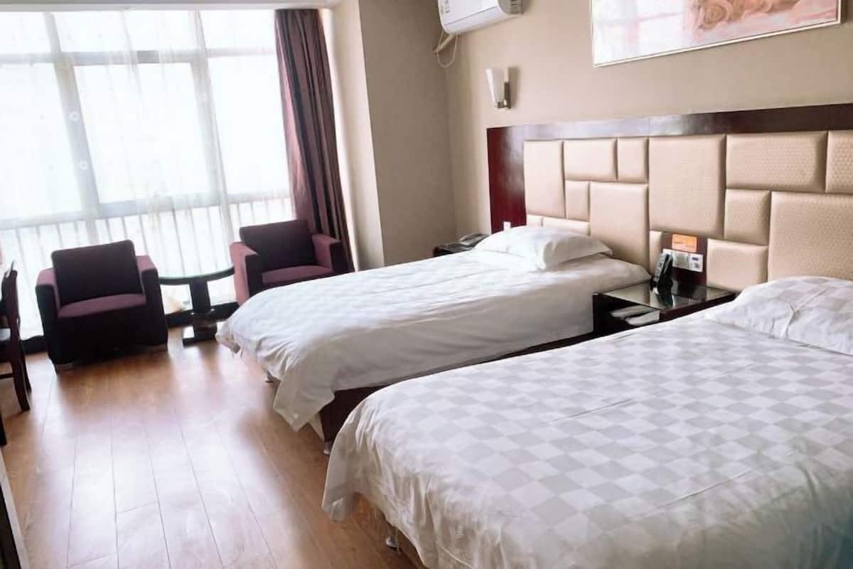 A hotel room with two beds, a small table, a chair, and a large window.