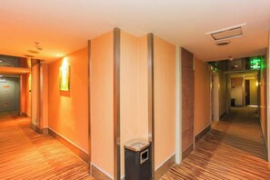 Ein Hotelgang mit Teppichboden, einem Mülleimer und einer Wandleuchte.