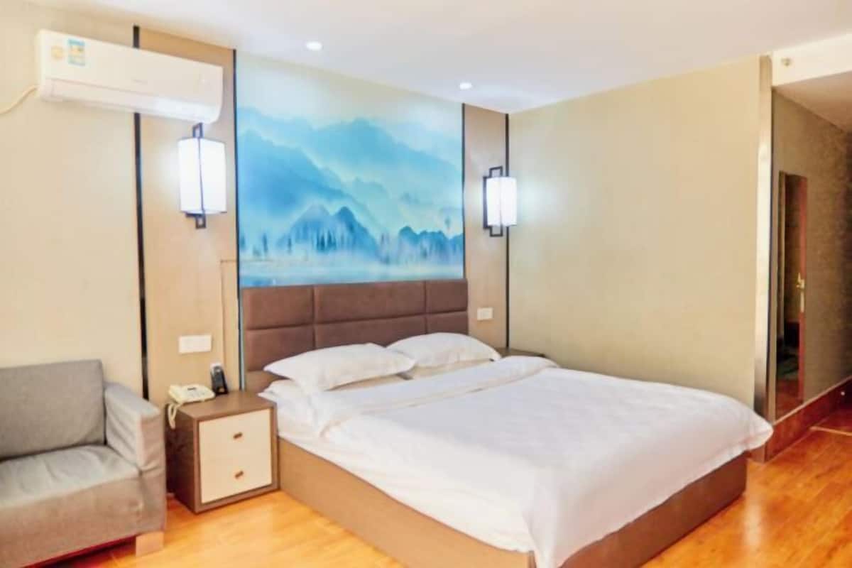 A hotel room with a bed, a nightstand with a phone, a sofa, and a wall-mounted air conditioner.