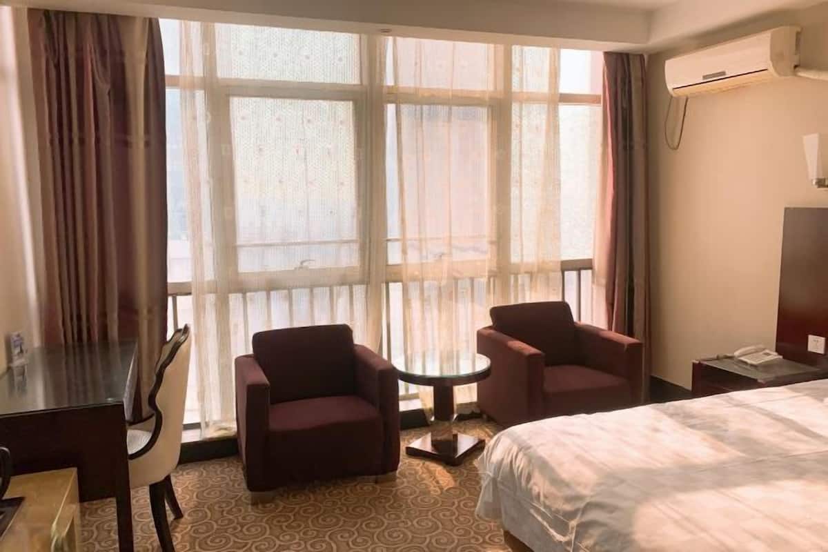A hotel room with a bed, two armchairs, a small round table, a desk, and a window with curtains.