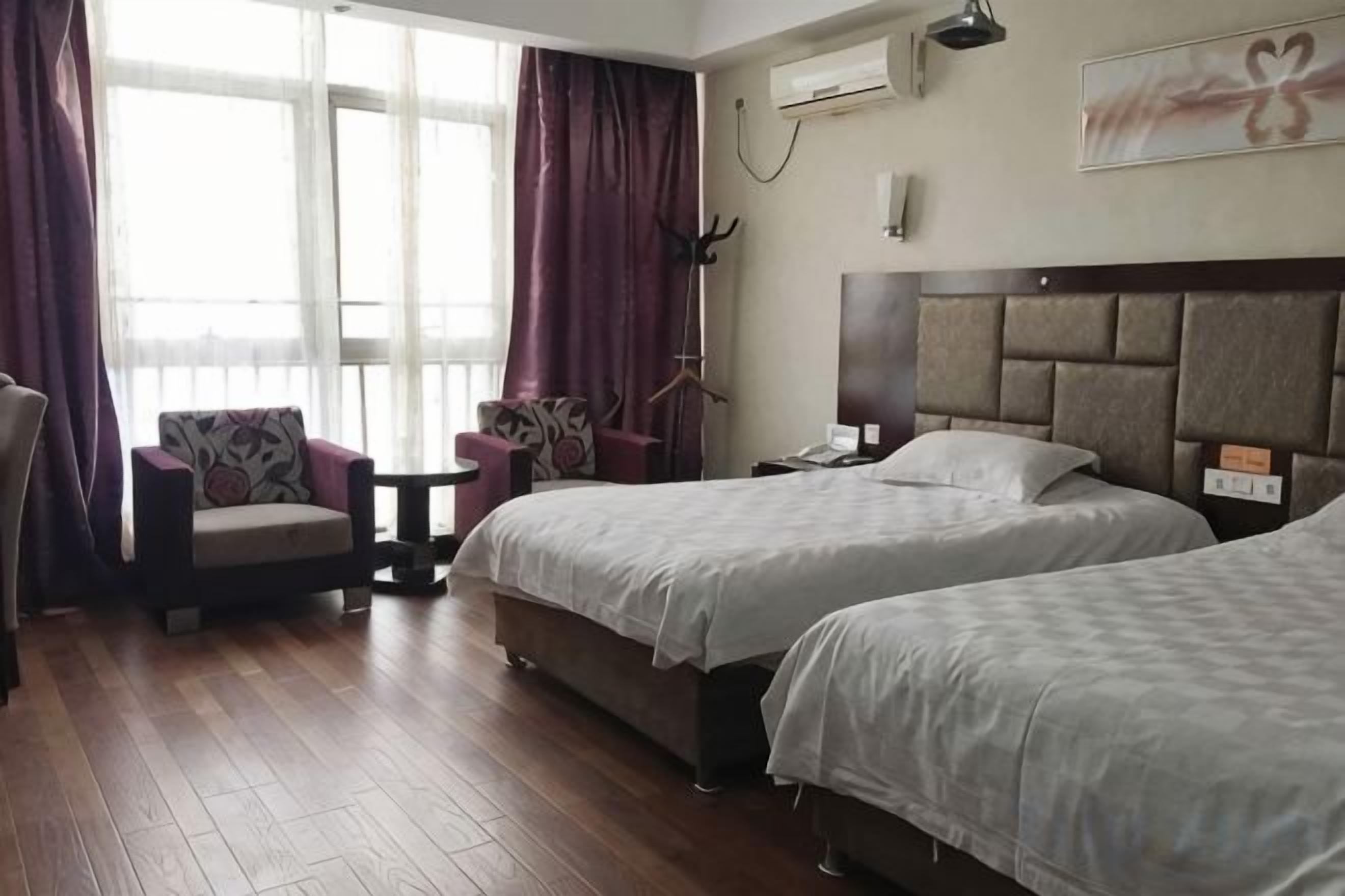 Una camera d'albergo con due letti, una sedia, un tavolino e una finestra con tende.