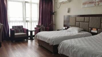Una camera d'albergo con due letti, una sedia, un tavolino e una finestra con tende.