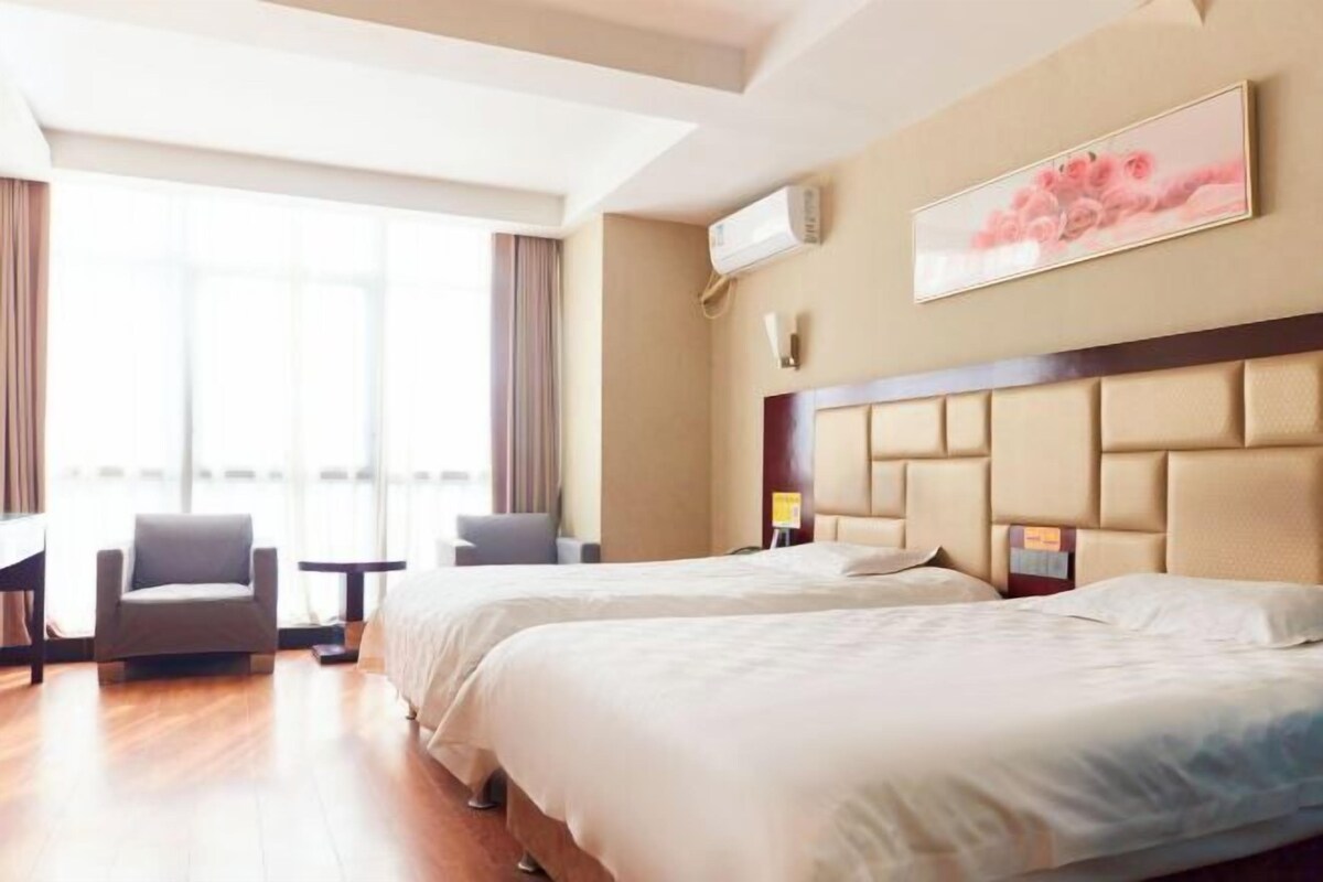 Habitación de hotel con dos camas, un escritorio, una silla y un ventanal grande.