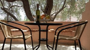 Un patio al aire libre con una mesa y dos sillas de mimbre, una botella de vino y un bol de fruta.