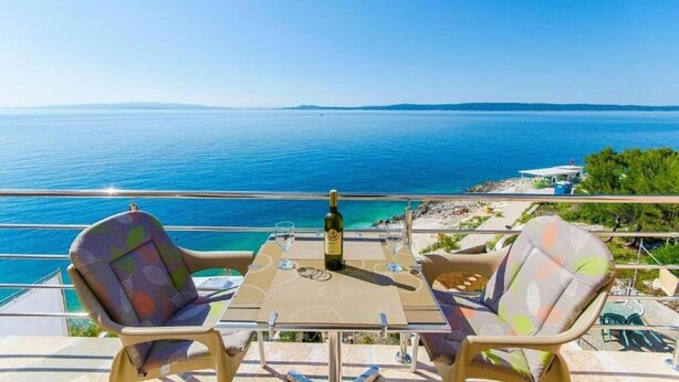 Een balkon met twee stoelen en een tafel, met uitzicht op een heldere blauwe zee.