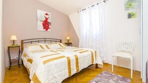 Een slaapkamer met een bed, twee nachtkastjes, een stoel, een raam met gordijnen en wanddecoratie.