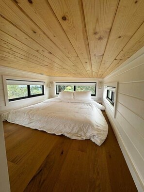 A bedroom with a wooden ceiling, a bed, and two windows.