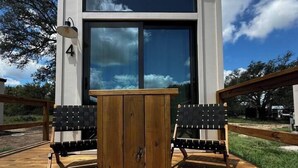 Een modern gebouw met grote ramen, een houten terras en twee zwarte stoelen.